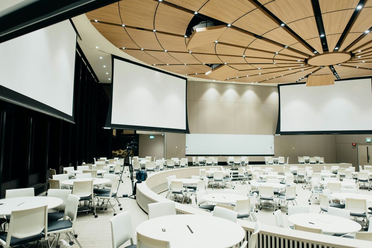 A large conference hall with round tables and projector screens